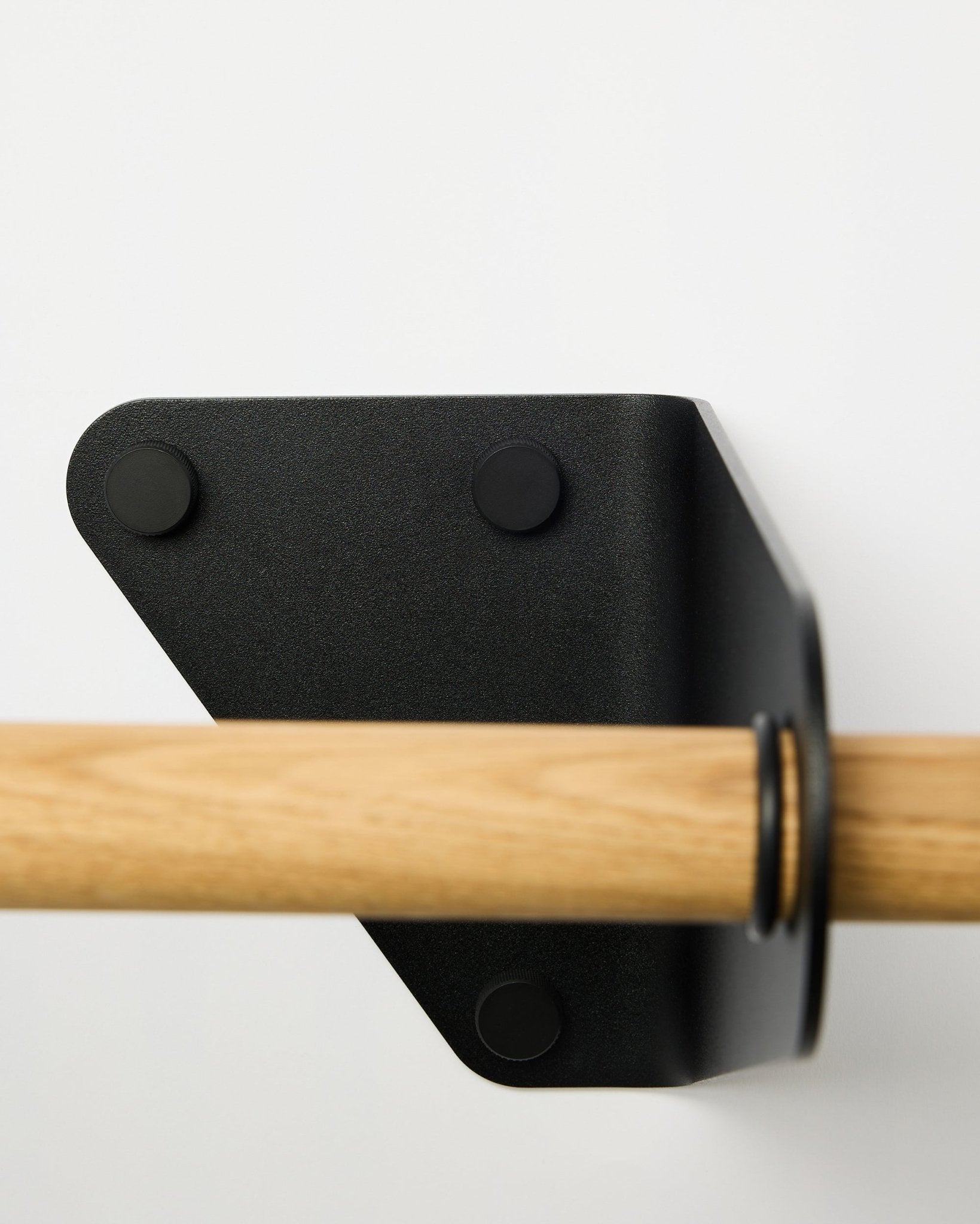 Plano aproximado do Linn Coat Rail da WoodUpp em black, 115,9 cm, instalado numa parede branca com um suporte metálico triangular, apresentado como parte da linha de acessórios acústicos nórdicos.
