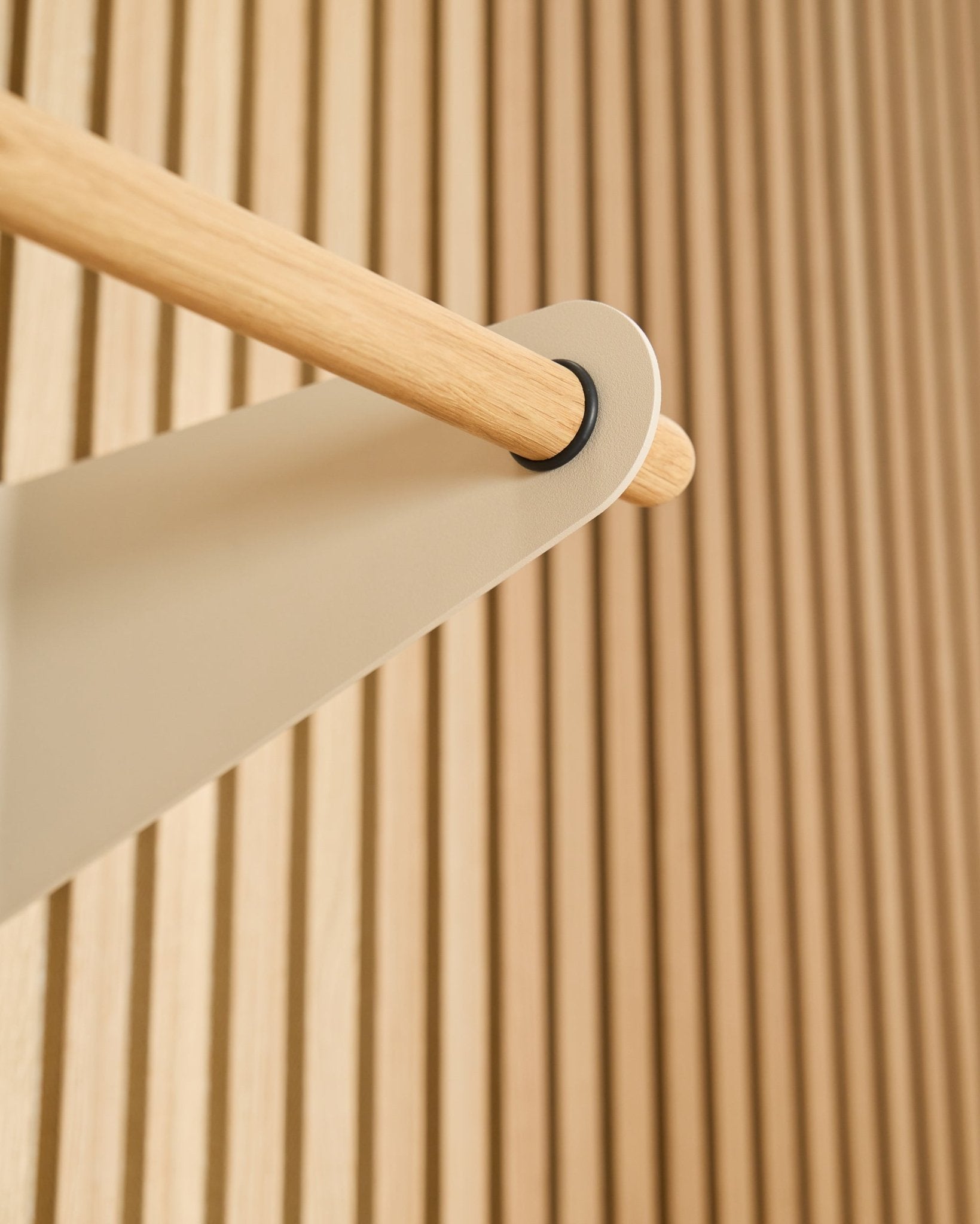 Grande plano do cabide WoodUpp Linn Coat Rail em beige (75,9 cm), montado num suporte metálico beige, contra um painel acústico ripado Akupanel texturado.