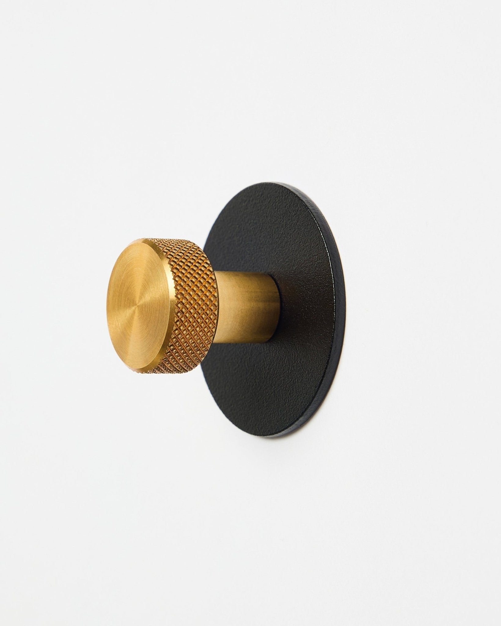 Gancho de parede Norr Coat Hook X1 da WoodUpp com botão texturado brass e base steel com revestimento a pó black, acessório para Akupanel, apresentado sobre fundo branco.