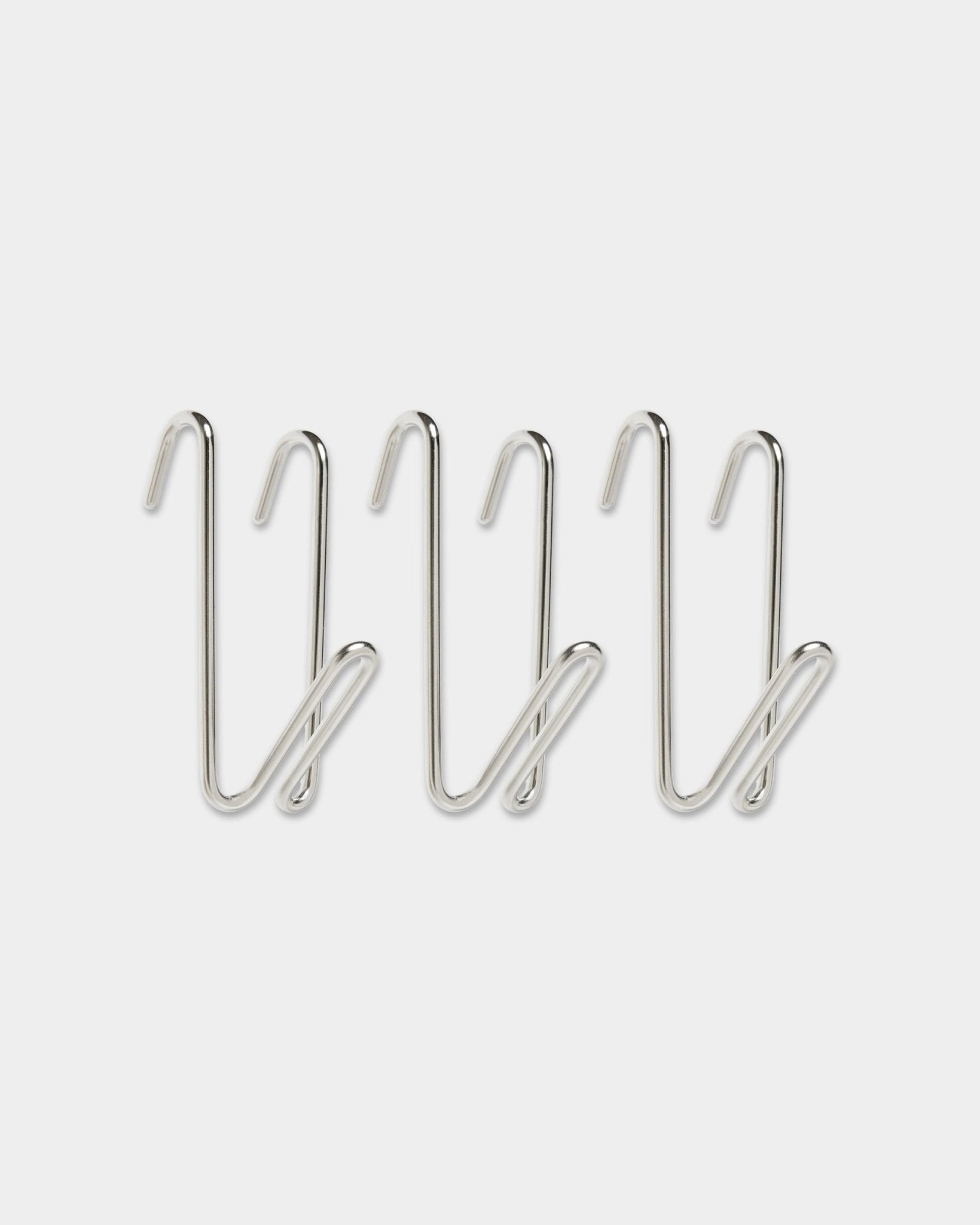 Três ganchos Alva Wire Hook / BM1, em aço inoxidável steel, tamanho curto da coleção CREATE da WoodUpp, com design em laço, alinhados em fila sobre um fundo branco liso.