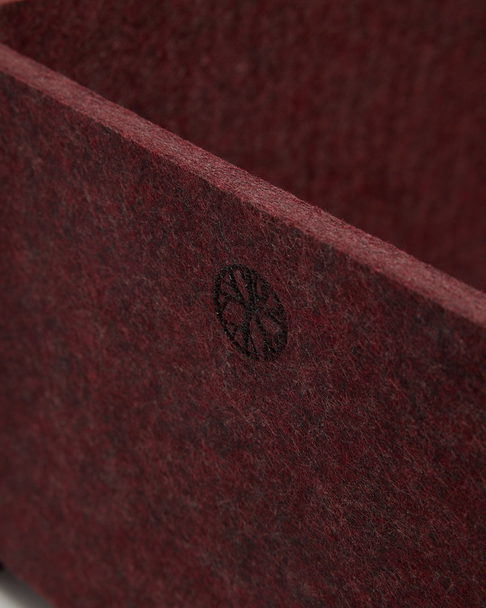 Grande plano da WoodUpp Vigg | Felt Box / BM2 em ox red, mostrando o feltro PET texturado e um emblema circular black no canto. Design nórdico de acessórios acústicos.