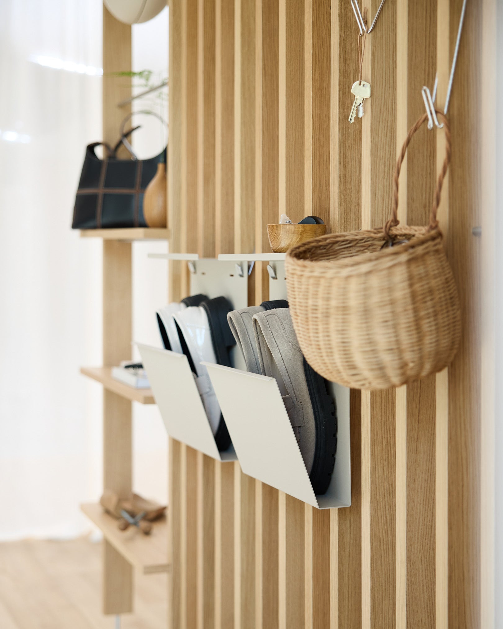 Hall de entrada moderno com o Nell Shoe Storage da WoodUpp em beige, paredes com painéis acústicos de madeira em Akupanel, ganchos de parede, um cesto suspenso e uma prateleira com peças decorativas expostas.