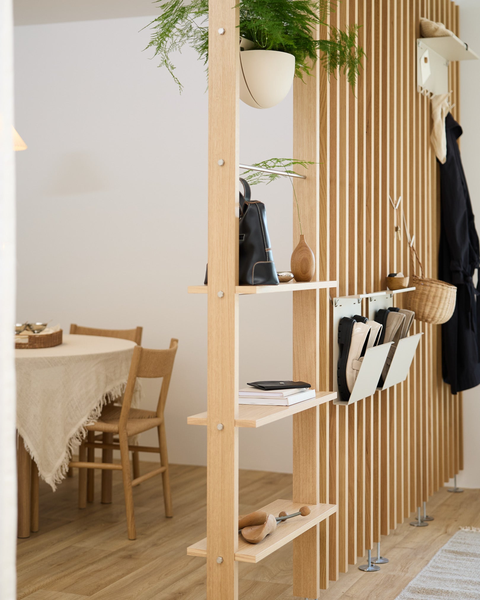 Uma estante aberta em madeira divide a zona de refeições e integra o Nell Shoe Storage em beige da WoodUpp, criando um espaço organizado para os sapatos numa casa nórdica moderna.