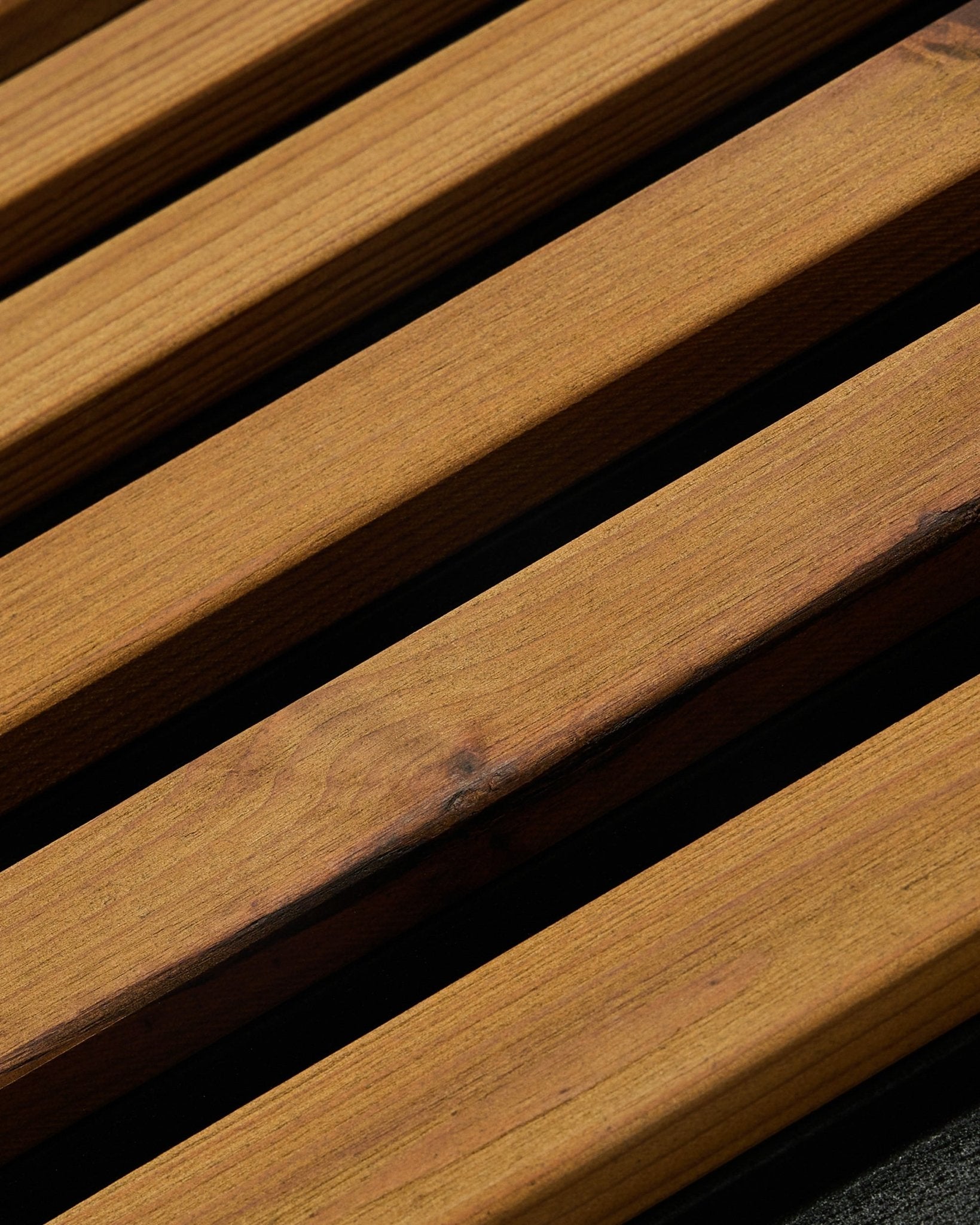 Pormenor do painel de fachada WoodUpp Aluwood em brown oleado (240 x 45,1 cm), em abeto nórdico termotratado, inclinado para mostrar as ripas com intervalos escuros entre elas.