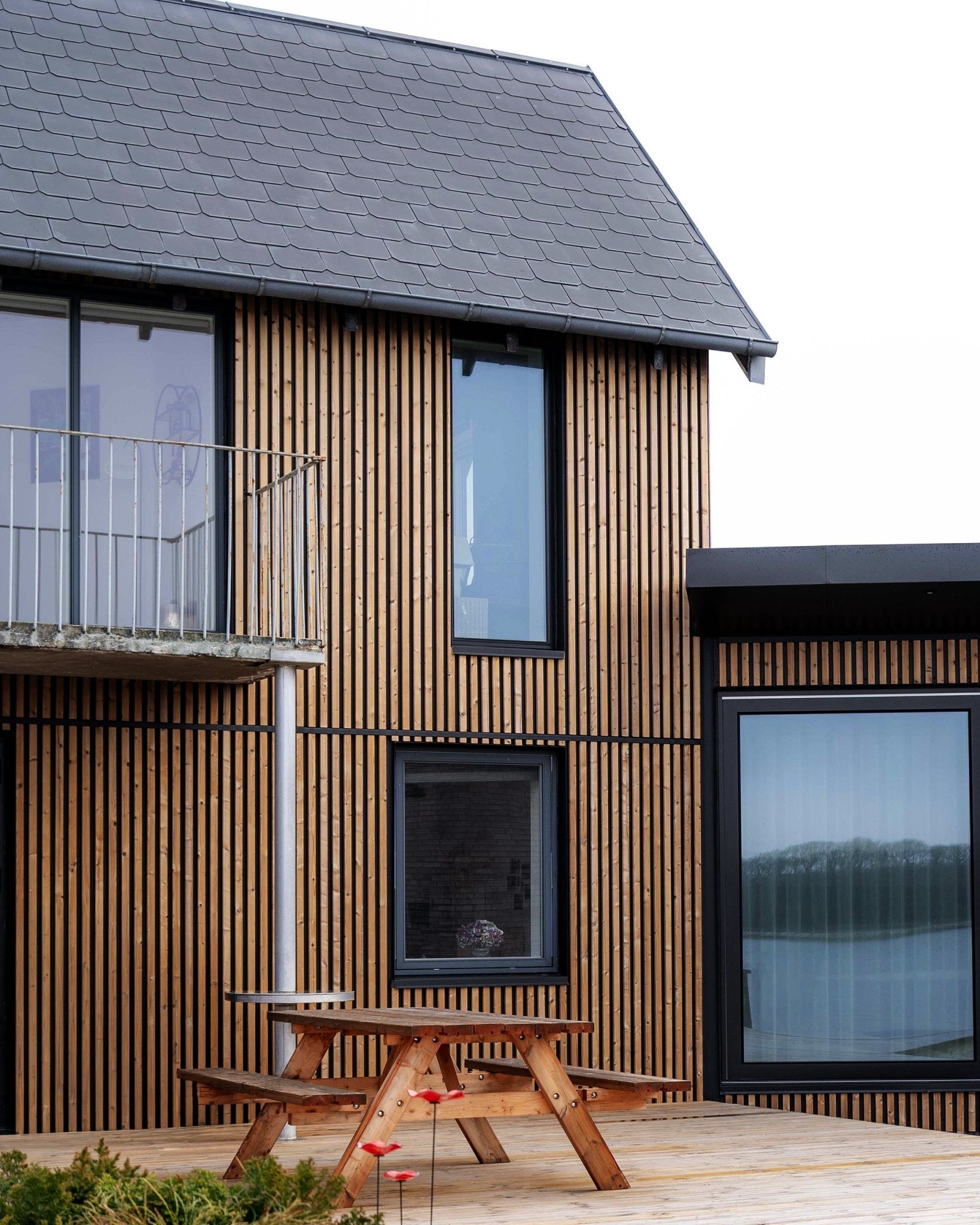 Casa moderna com painéis de fachada WoodUpp Aluwood em Brown oleado, com janelas large, uma varanda e um deck com mesa de piquenique em madeira.
