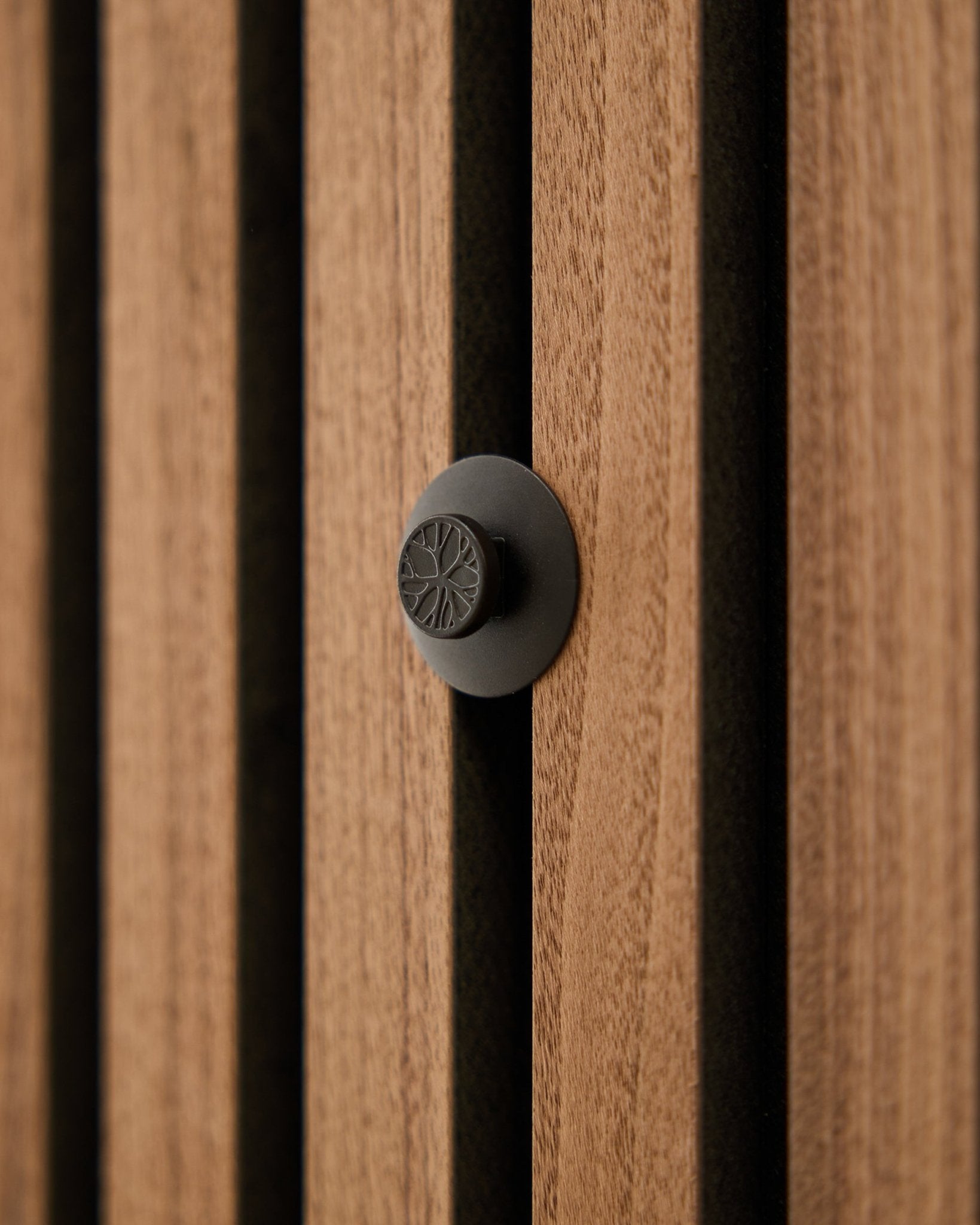 Grande plano de um botão redondo black do conjunto WoodUpp Dupps Original, instalado numa moderna parede acústica de ripas de madeira vertical Akupanel.