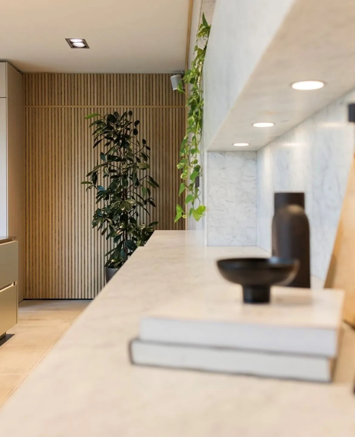 Um interior moderno com uma prateleira de mármore, objetos decorativos, plantas verdes e uma parede de painel de madeira acústica nórdica Akupanel ao fundo.
