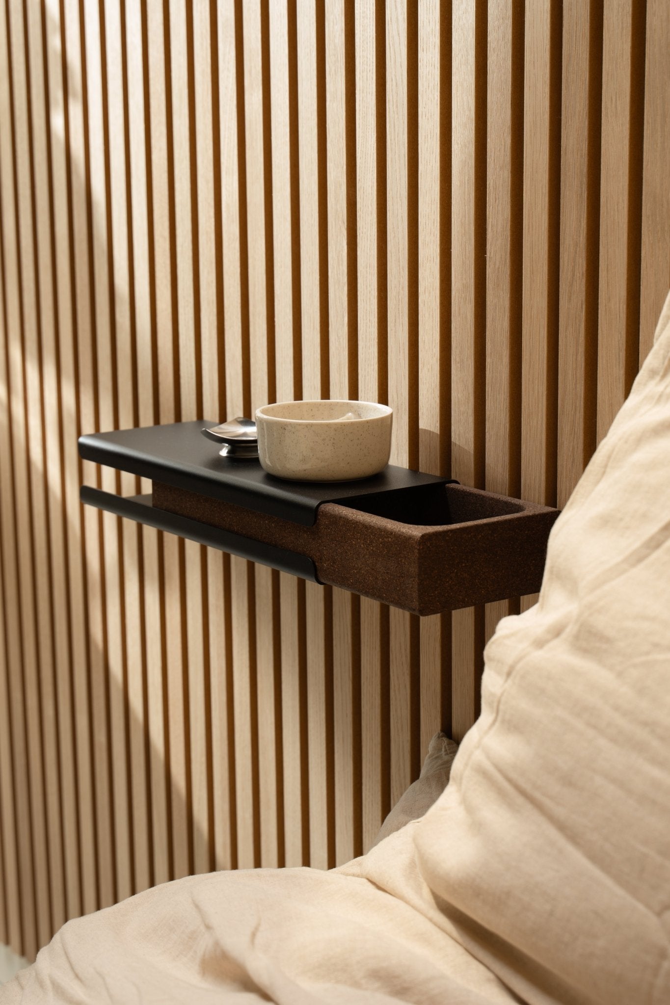 Prateleira de parede minimalista com uma taça de cerâmica e o acessório WoodUpp Norr Key Tray ao lado de uma almofada beige e de Akupanel Painel acústico, iluminada por uma luz natural suave.