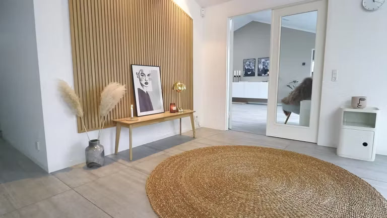 Sala de estar nórdica minimalista com um tapete redondo de juta, banco de madeira com grama dos pampas, arte emoldurada e uma parede de destaque de madeira acústica Akupanel ripada.