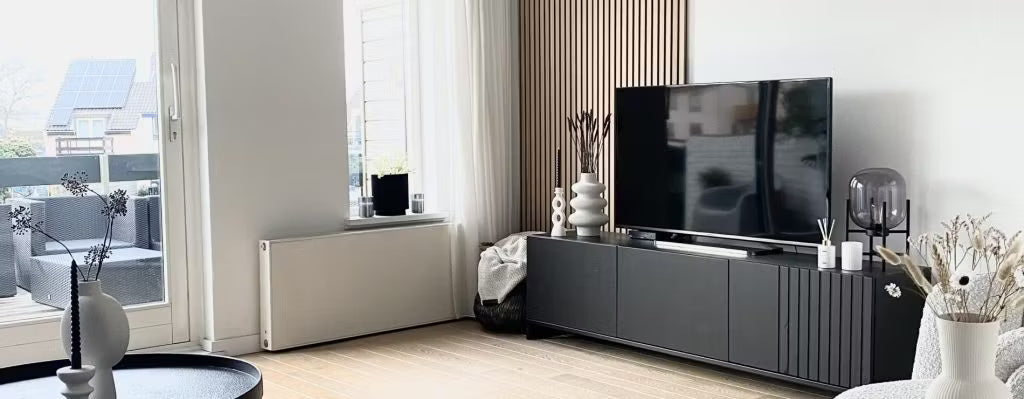 Sala de estar moderna com um suporte de TV preto, TV de tela plana, vasos decorativos e janelas grandes com luz natural e vista para o pátio; Akupanel em uma parede.