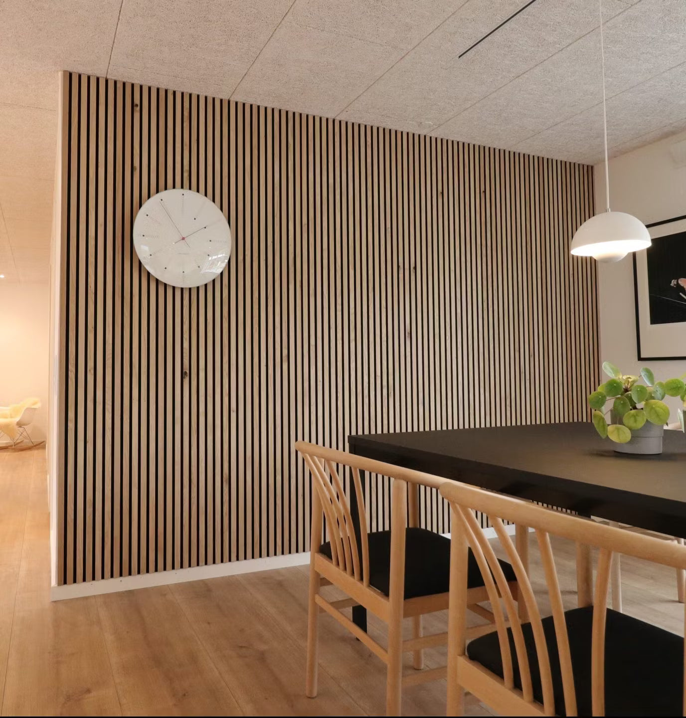Sala de jantar moderna com uma parede nórdica de ripas de madeira acústica Akupanel, mesa preta, cadeiras de madeira com assentos pretos e um centro de mesa com vasos de plantas.