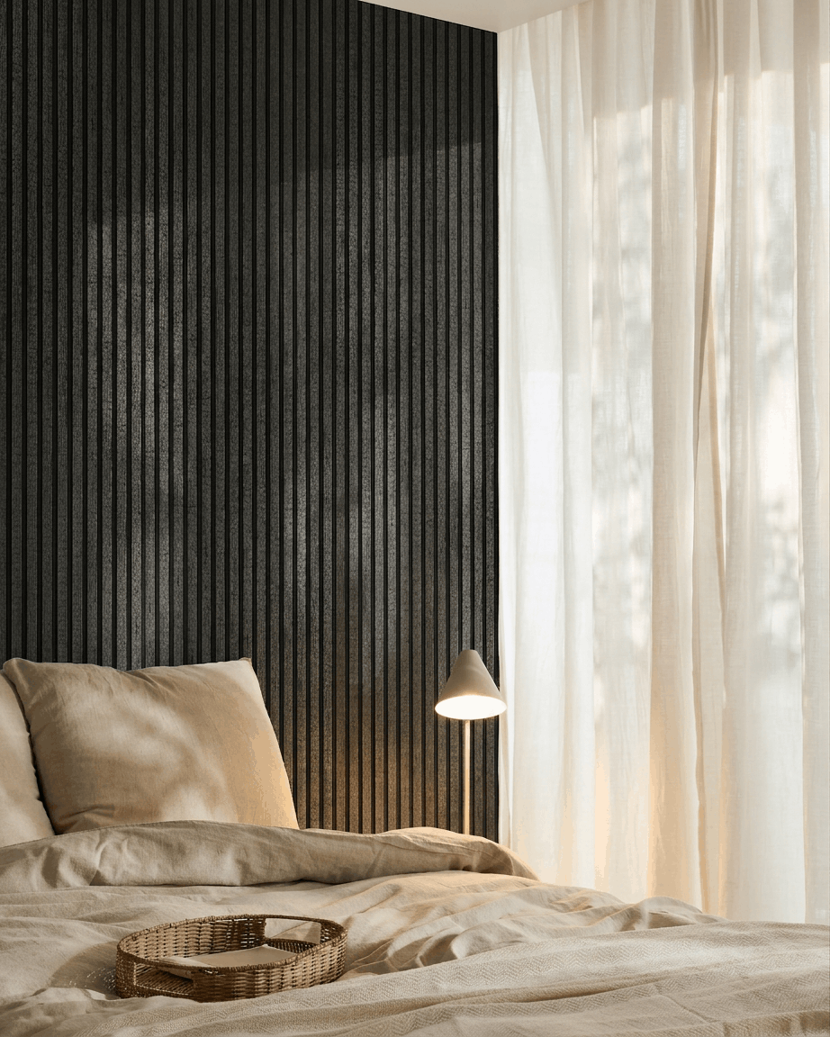 Quarto acolhedor com roupa de cama beige, uma bandeja em vime, candeeiro branco, cortinas translúcidas e um painel acústico de madeira WoodUpp Akupanel em charcoal montado na parede.