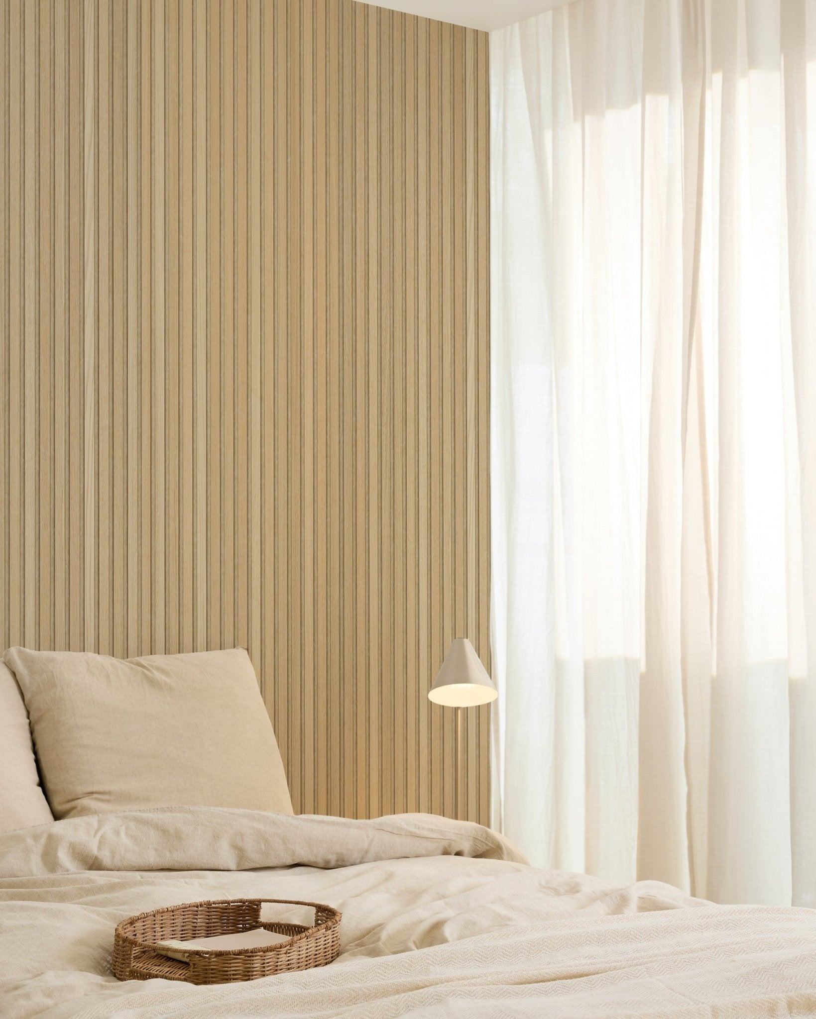 Quarto minimalista com roupa de cama beige, um tabuleiro em verga, candeeiro de parede moderno, parede de destaque em painel acústico de madeira Akupanel e cortinas translúcidas que filtram suavemente a luz natural.