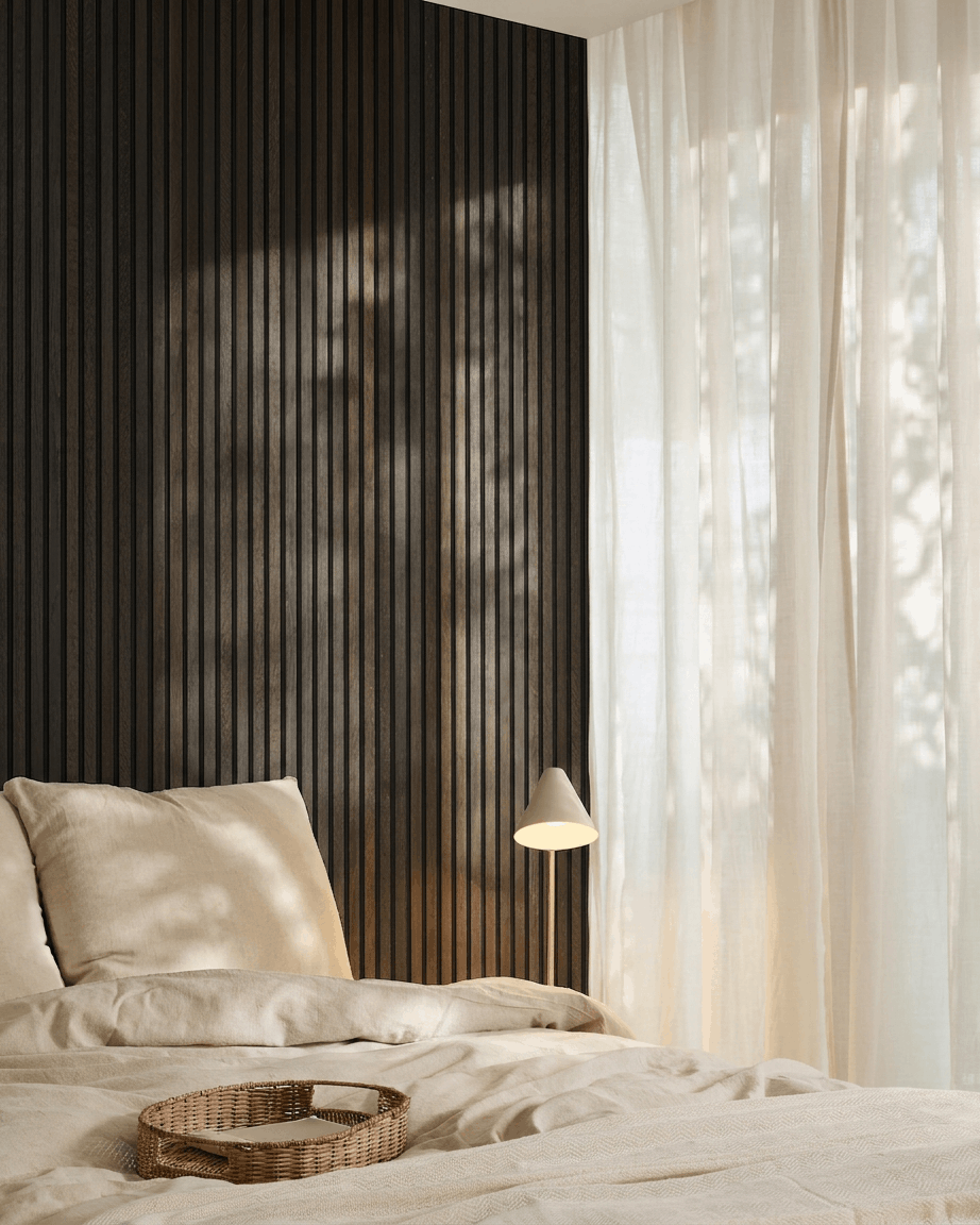 Quarto minimalista com uma cama <span data-glossary-id="0eef722625fb5e8b939816fa4eb65993">off-white</span>, tabuleiro de vime, apontamentos Scandi e painel acústico de madeira <span data-glossary-id="ad1a5fcbab757c8ac4796572d9a9084c">AcousticPanel</span> da WoodUpp em Rustic <span data-glossary-id="f1e199c421268630e73c2f89e57350a4">Black</span>, montado numa parede escura.