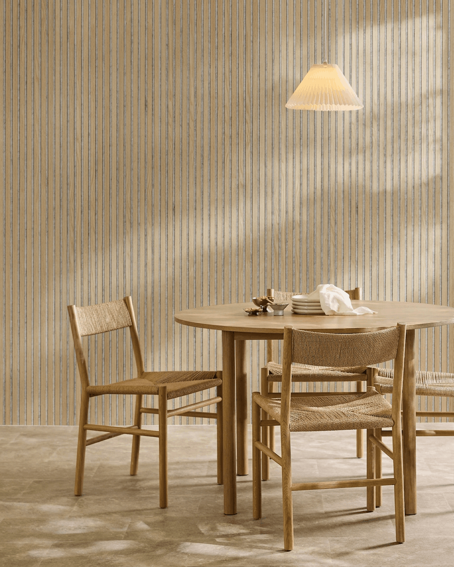 Sala de jantar minimalista com mesa redonda de madeira, cadeiras em vime, um candeeiro suspenso e um painel acústico em madeira WoodUpp Akupanel em Carvalho Clássico com feltro grey.