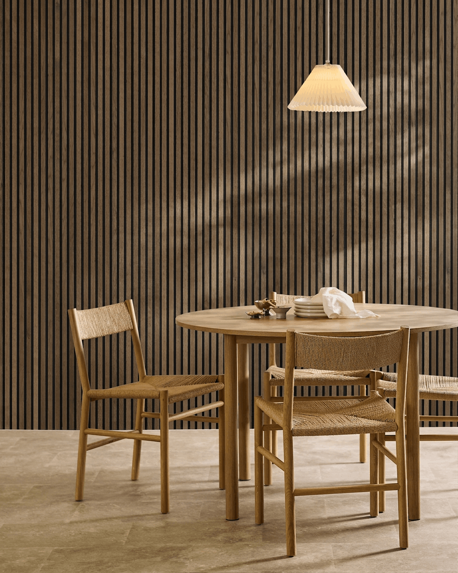 Zona de jantar minimalista com mesa redonda, cadeiras em vime e candeeiro suspenso, com um painel acústico de ripas WoodUpp Akupanel Rustic Grey Oak.
