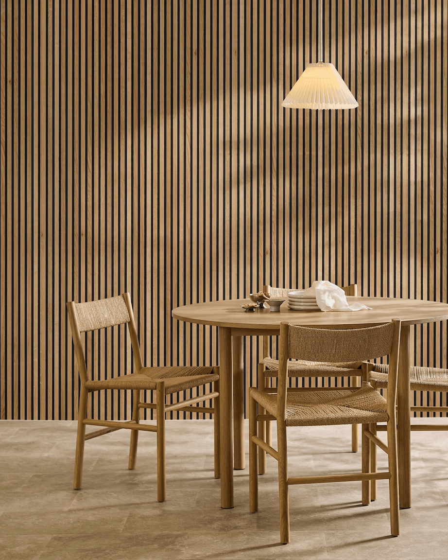 Zona de refeição minimalista com mesa redonda, cadeiras entrançadas e painel acústico ripado WoodUpp Akupanel em Rustic Natural Oak como destaque de parede nórdico.