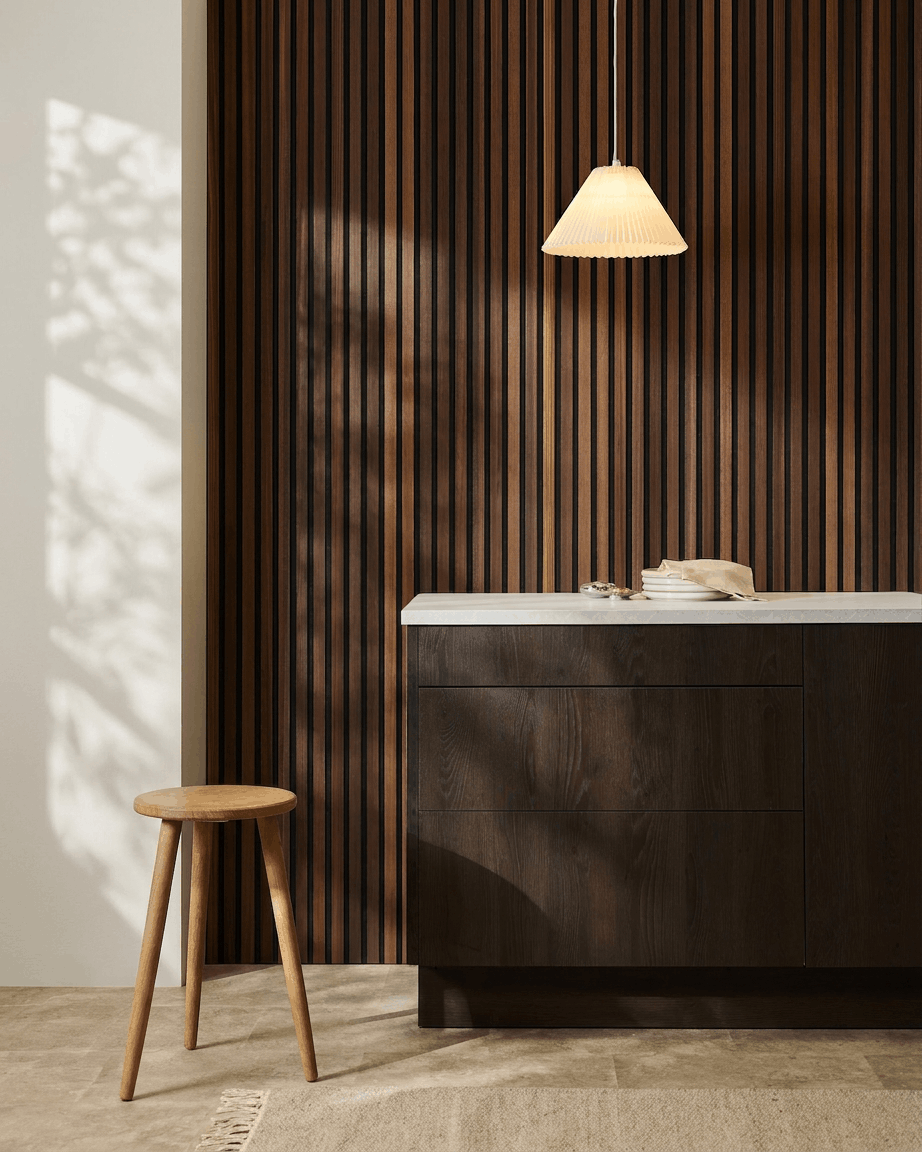 Interior minimalista com um banco de madeira, armário em madeira escura, candeeiro suspenso e um painel acústico de ripas de madeira WoodUpp Akupanel em Natural Wood/larício fumado.