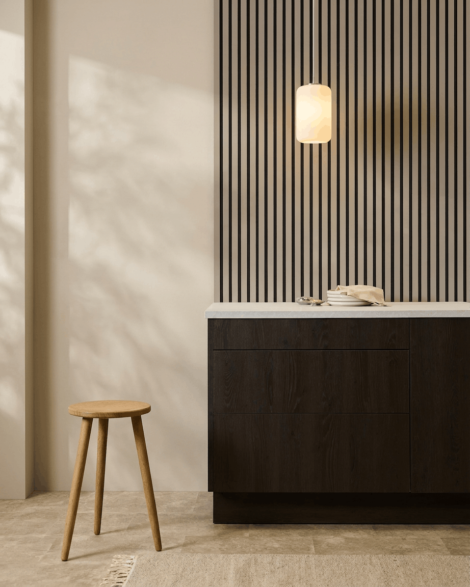 Cozinha minimalista com painéis acústicos WoodUpp Akupanel (Stone, feltro Black) na parede, banco de madeira, armários escuros e candeeiro suspenso em tons neutros.