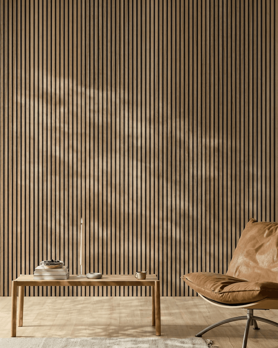 Sala minimalista com um WoodUpp Akupanel Painel acústico (ripas em Nogueira Inglesa, feltro black), cadeira em pele castanha, mesa em madeira clara, vela, livros, chávena e tapete branco à luz do sol.