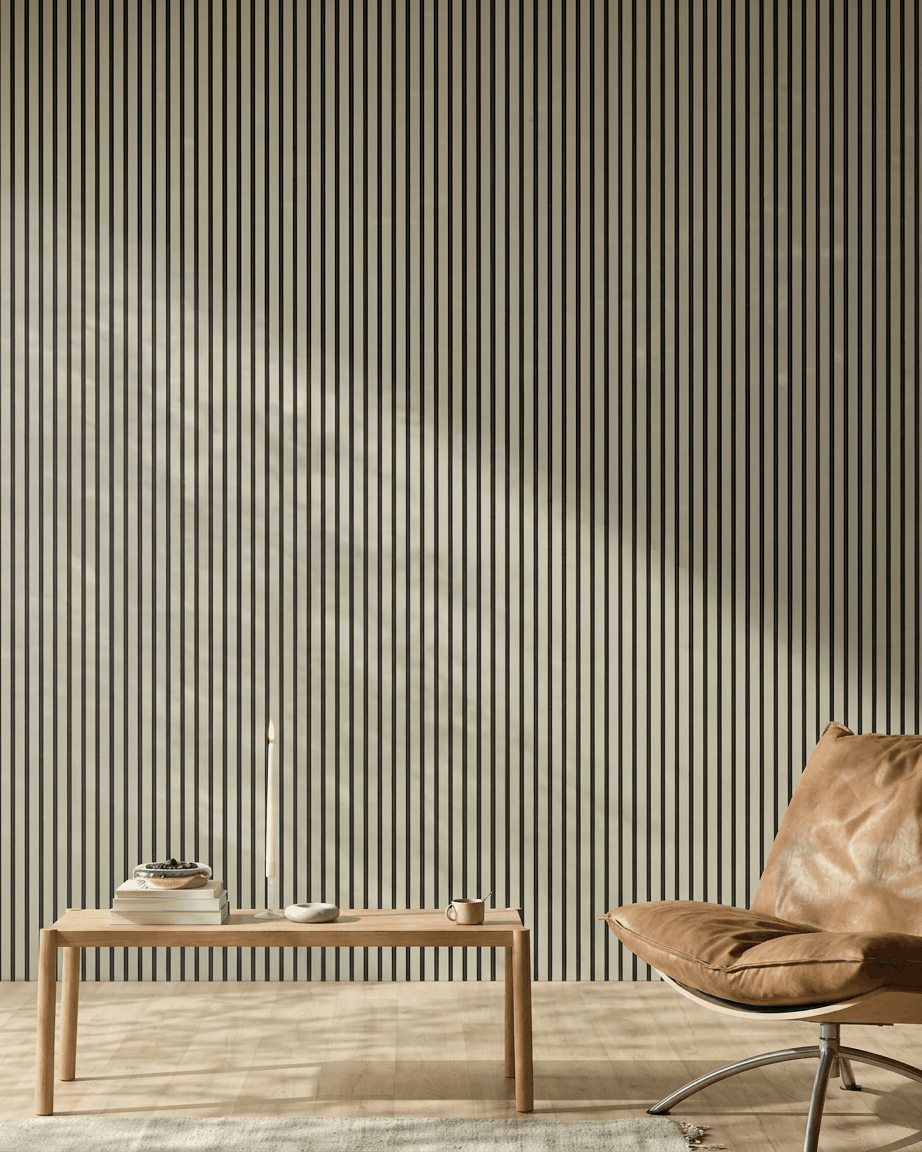 Sala minimalista com uma cadeira em pele castanha, banco de madeira, livros, vela e o Akupanel Stone/Black Felt Painel acústico da WoodUpp (240x60 cm) na parede.