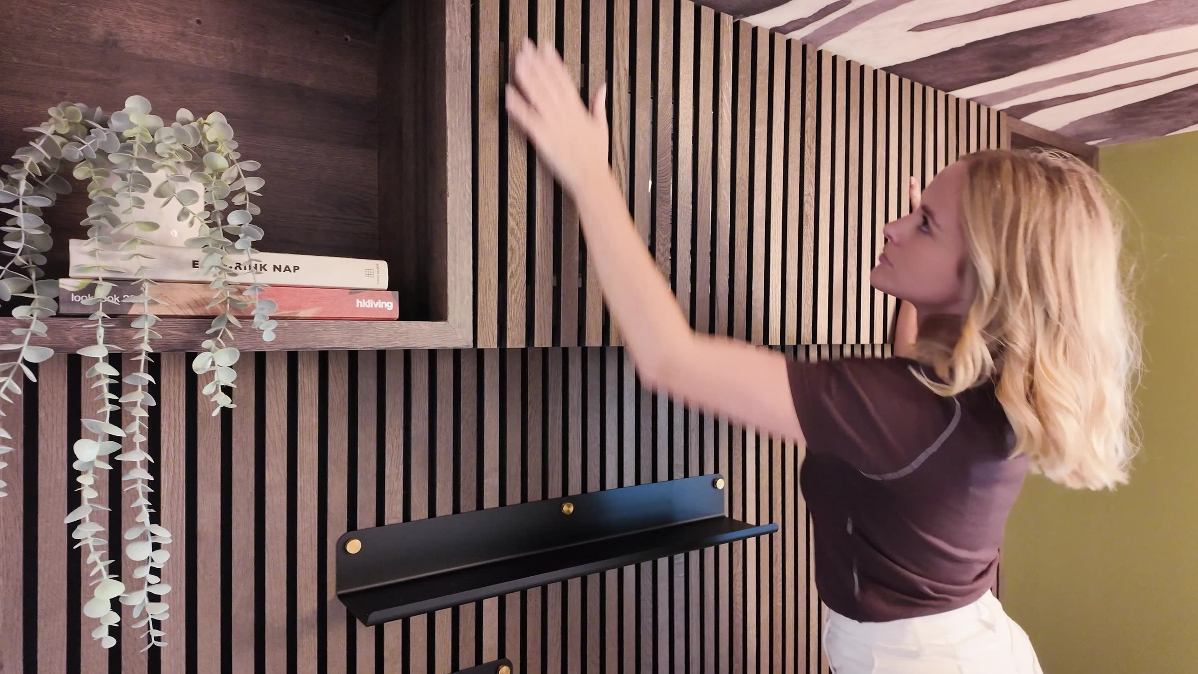 Woman fitting a slat grille over the air conditioner in a slatted bedroom wall