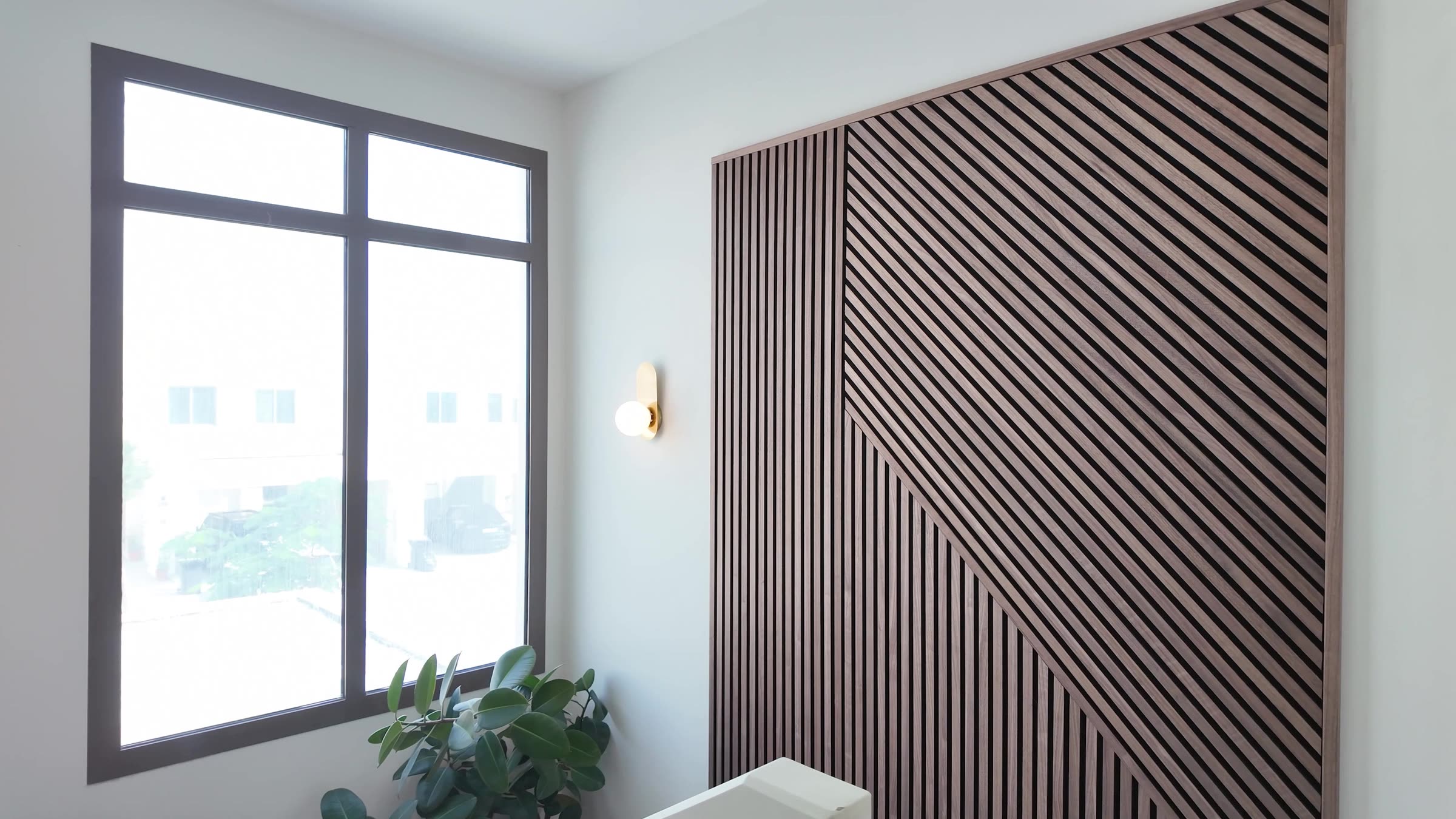 Wide view of a stairwell wall with a framed Akupanel slat artwork next to a window and a rubber plant