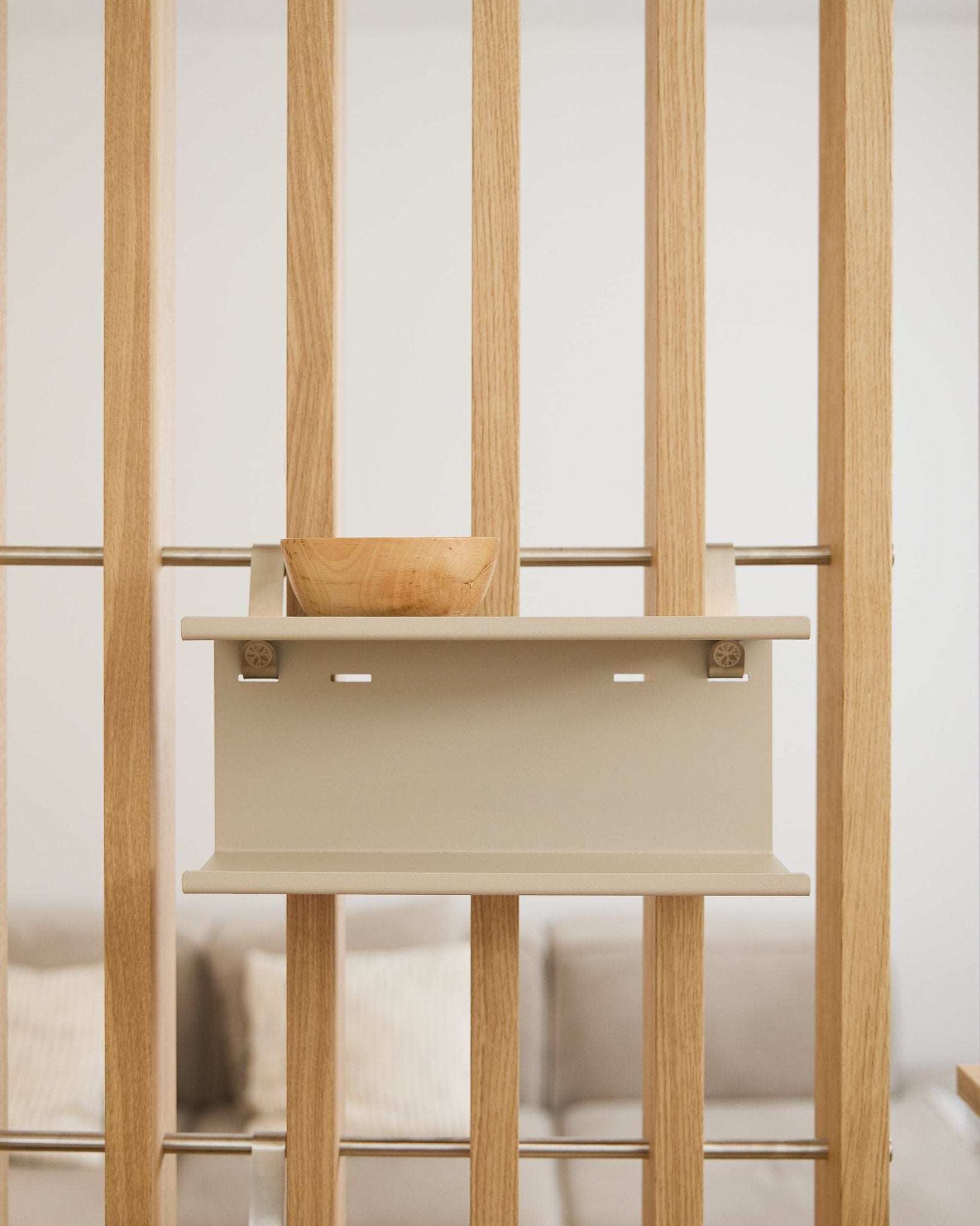 Uma taça de madeira small sobre a beige Nell Double Metal Shelf da WoodUpp (31,7 cm), com um sofá e almofadas desfocados ao fundo.