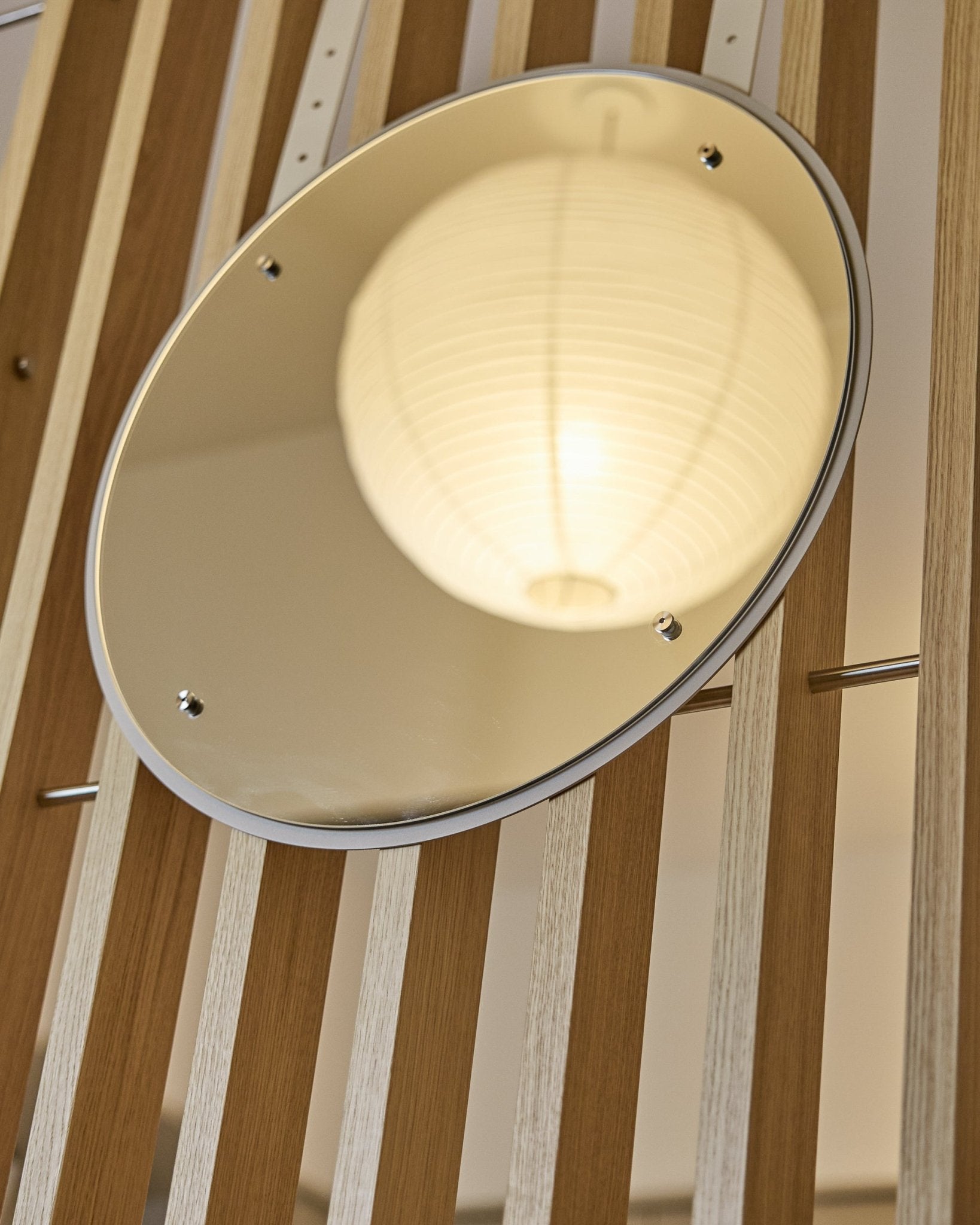 O Vala | Mirror / BM1, D54 cm da WoodUpp é um espelho redondo com altura regulável, montado em painéis acústicos ripados vertical, que refletem uma lanterna de papel iluminada.