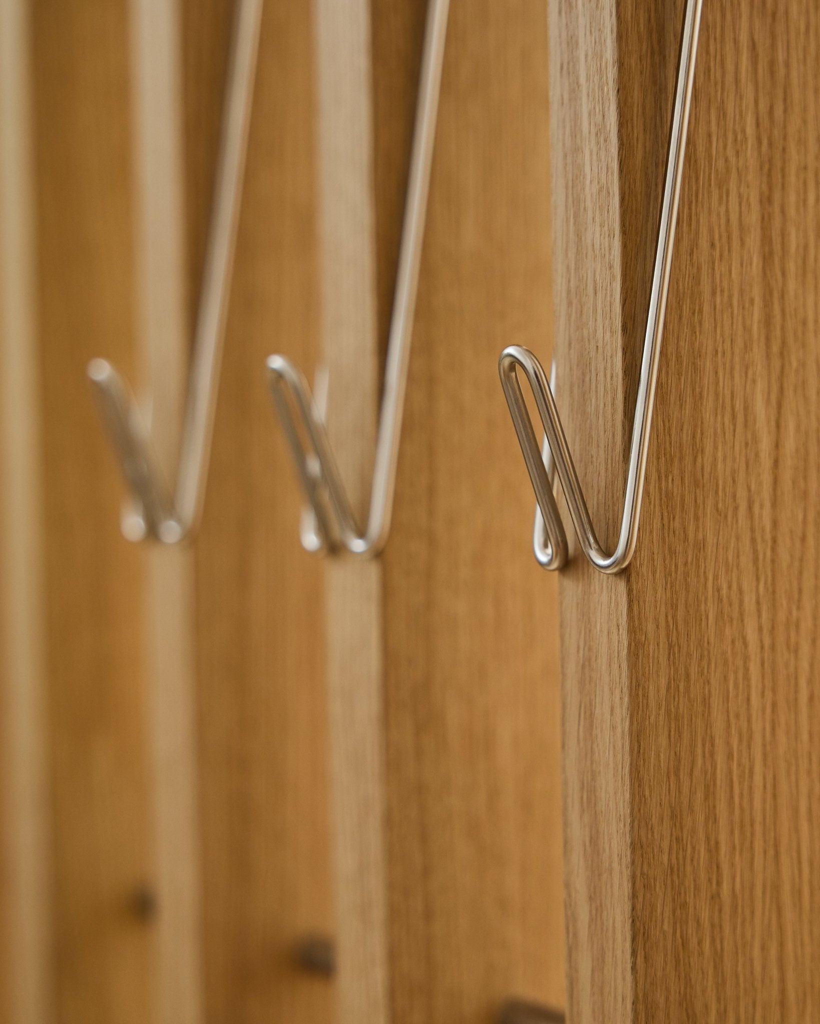 Grande plano de três Alva | Wire Hook / BM1, aço inoxidável Steel, compridos, da WoodUpp, montados em fila sobre painéis acústicos de madeira Akupanel e a projetar sombras suaves.