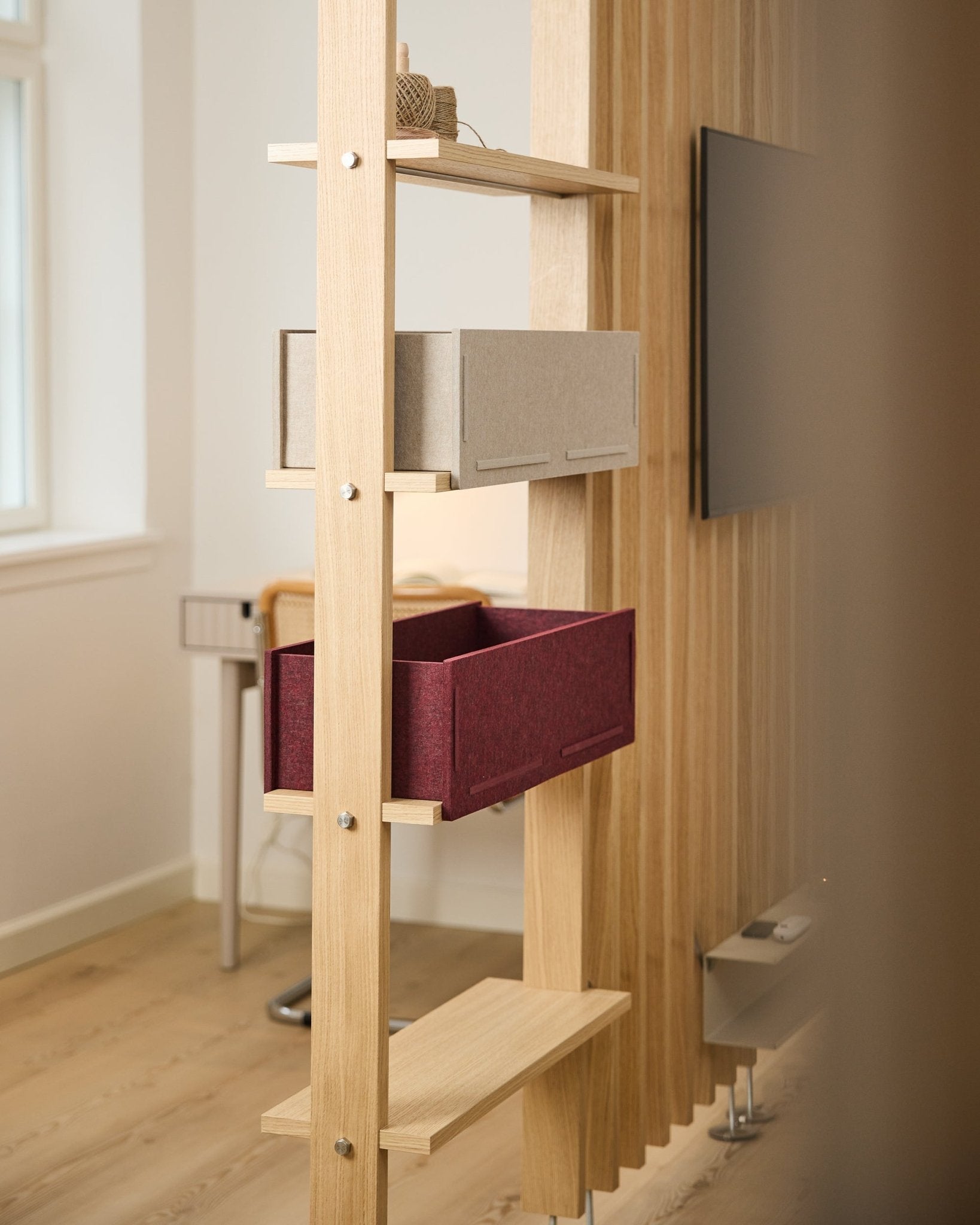 Uma prateleira da WoodUpp apresenta uma caixa de arrumação beige e uma Vigg Felt Box / BM2 ox red, numa divisão nórdica luminosa e minimalista com detalhes acústicos em madeira.