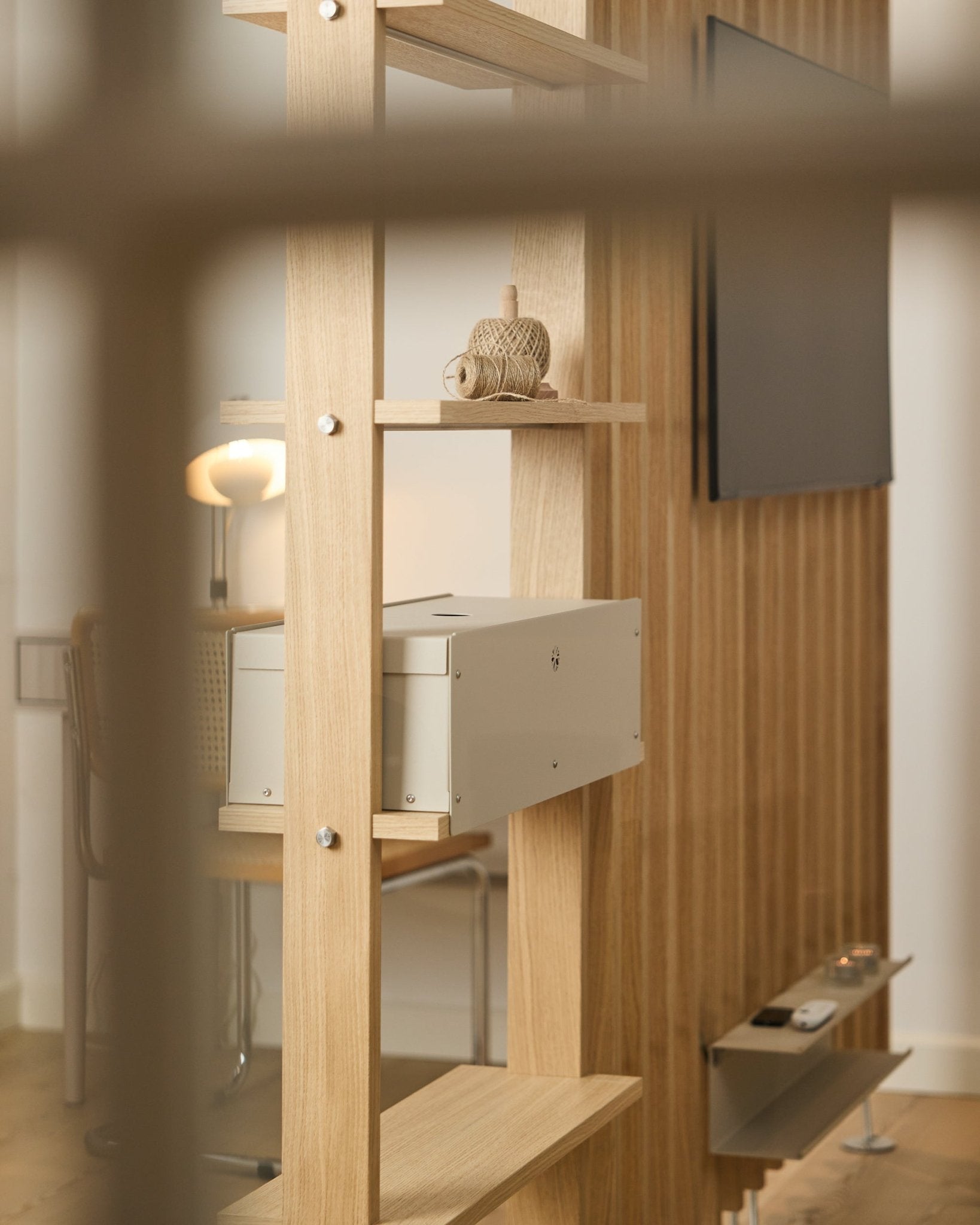 Uma divisão acolhedora com cadeira, candeeiro e televisão apresenta a prateleira Nell | Metal Box / BM2 da WoodUpp, com acabamento em beige e decoração nórdica minimalista.