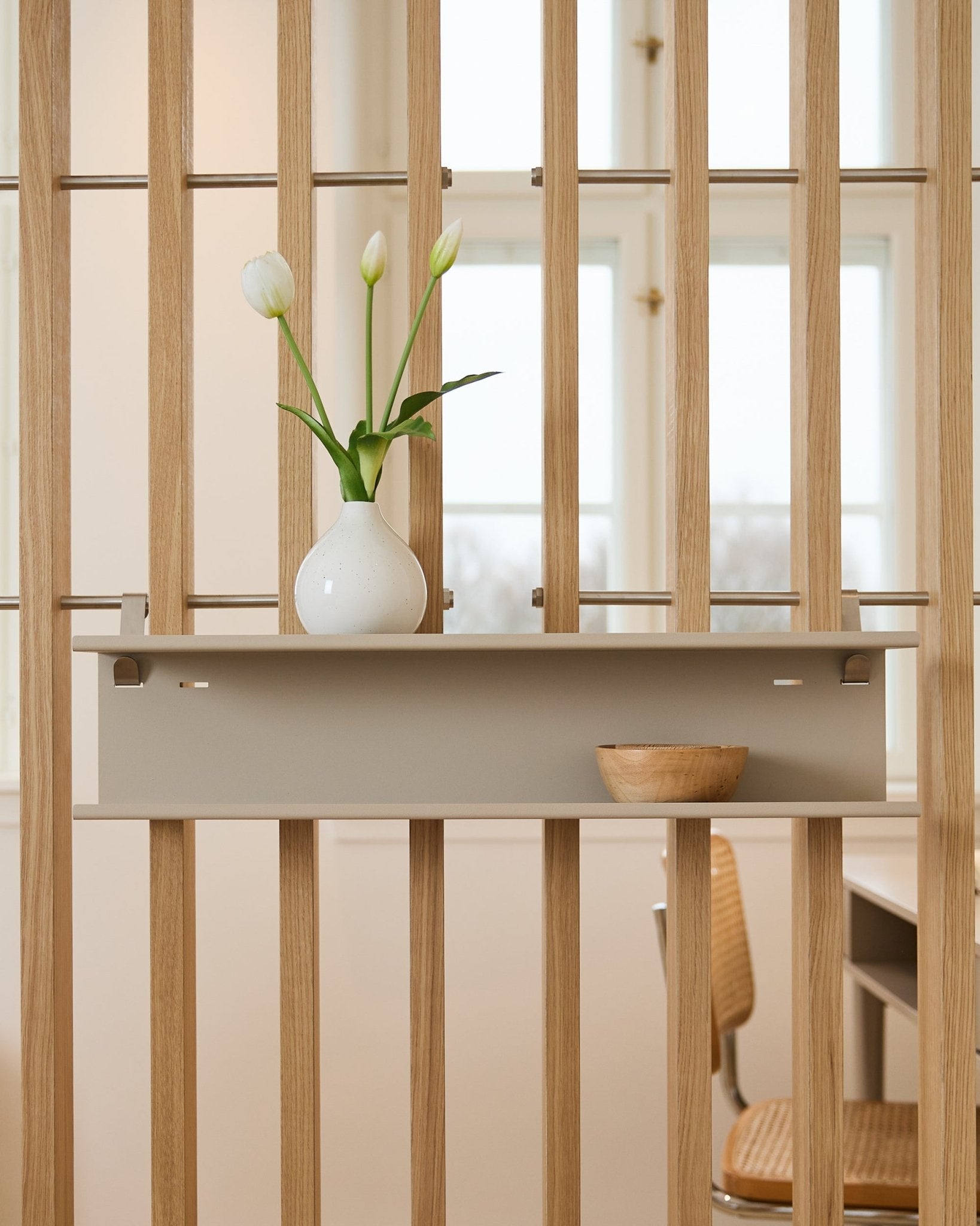Prateleira Metálica Dupla / BM1 da WoodUpp em beige (63,5 cm), montada num divisor de espaços ripado, decorada com uma jarra e uma taça de madeira.