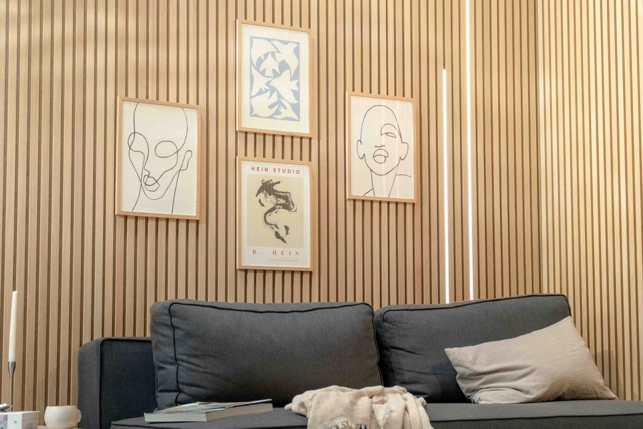 Sala de estar moderna com um sofá escuro com almofada bege, acentuado por uma parede nórdica de ripas de madeira acústica Akupanel e arte escandinava minimalista acima.