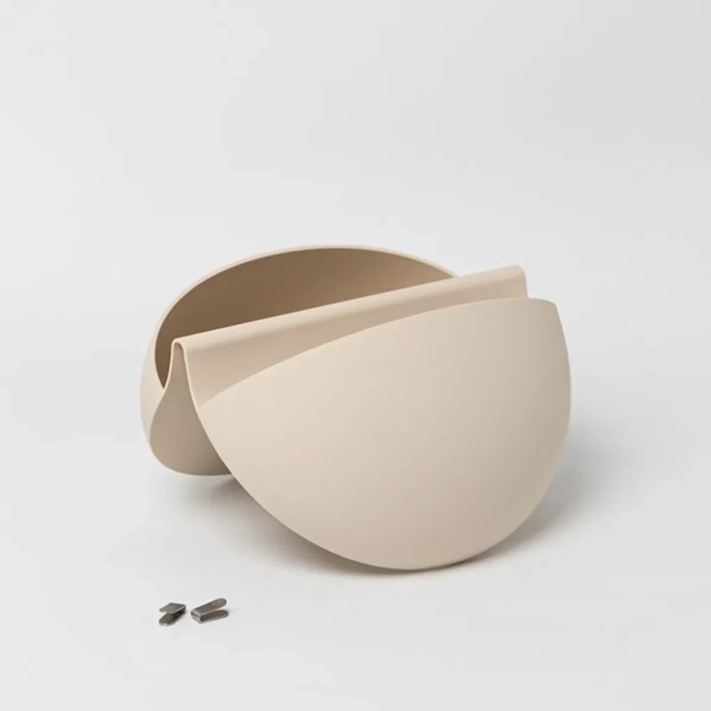 Floreira de parede WoodUpp em acabamento bege, formada por duas conchas semicirculares encaixadas que criam um recipiente curvo para plantas; acompanha dois pequenos ganchos metálicos de fixação visíveis à frente. Design minimalista e modular, com bordas suaves e superfície fosca.