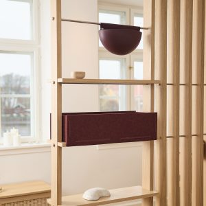Estante/biombo modular de madeira da WoodUpp com caixa organizadora de feltro bordô encaixada numa prateleira e vaso semiesférico suspenso bordô da WoodUpp pendurado em haste metálica; pequenos objetos decorativos — cumbuca de madeira e pedra branca — sobre as prateleiras.