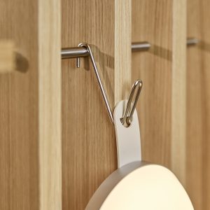 Painel de madeira de carvalho com trilho e ganchos metálicos da WoodUpp, mostrando um gancho de aço apoiando uma luminária portátil circular da WoodUpp com alça branca. Detalhe do acabamento em madeira, superfície fosca da lâmpada e fixação prática para pendurar acessórios.