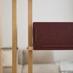 Divisória modular WoodUpp em ripas de carvalho claro com encaixes metálicos, acompanhada de um painel retangular de feltro bordô preso à estrutura. A imagem mostra textura do feltro, detalhes das emendas em madeira e o design minimalista e funcional do produto WoodUpp.