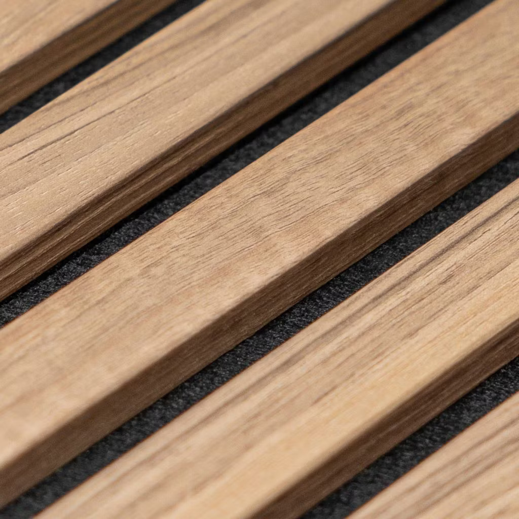 Close-up de painel acústico WoodUpp: ripas de madeira natural claras, tonalidade quente e acabamento mate, perfil retangular com arestas levemente chanfradas. Dispostas em linhas paralelas sobre base de tecido preto acústico, mostram veios, textura e vãos regulares, enfatizando qualidade e padrão repetitivo do produto WoodUpp.