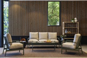 Interior com parede revestida por painéis ripados de madeira WoodUpp, janela estreita e estante modular WoodUpp em madeira clara com vasos e copos. Ambiente com sofá e duas poltronas de estrutura verde e almofados bege, mesa de centro e tapete neutro, iluminação natural.